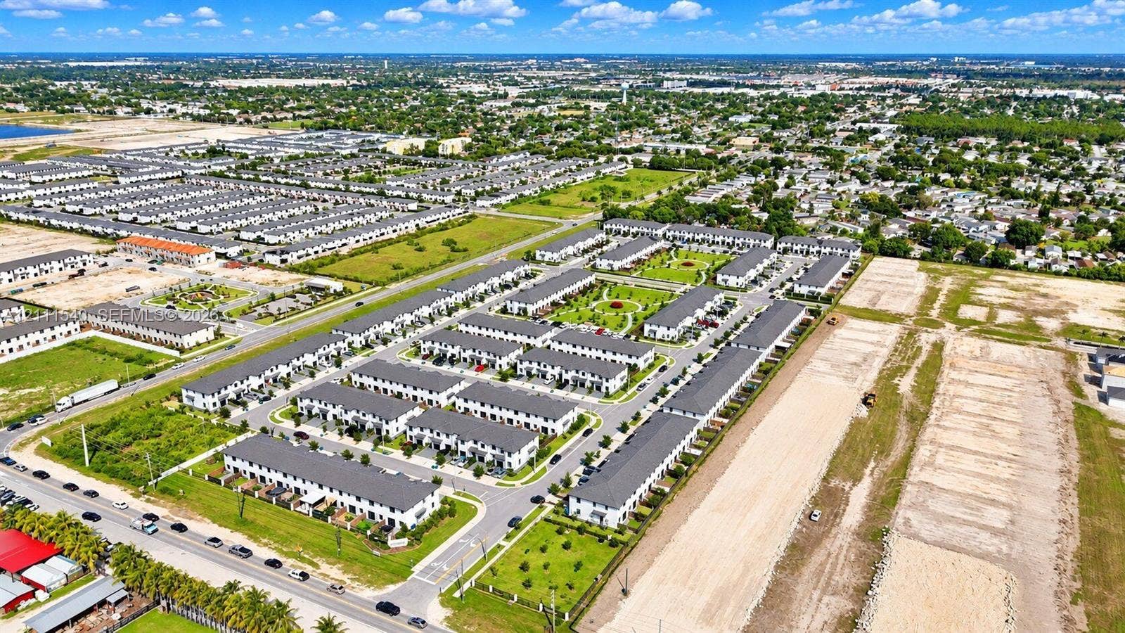 Aerial perspective of a multi-unit residential community featuring asphalt roadways, structured perimeter landscaping, uniform roofing, and paved sidewalk systems