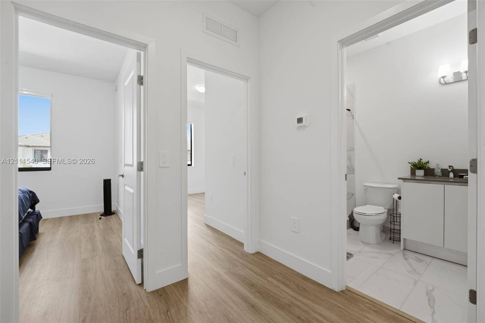 Wood-finish flooring throughout, white interior doors, and a bathroom featuring a vanity with a countertop, a wall-mounted light fixture, and tile flooring