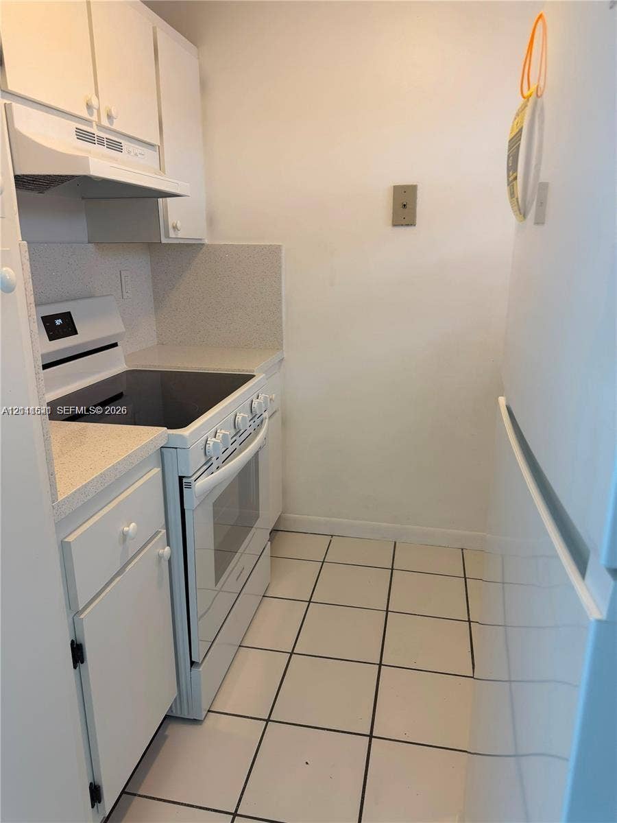 Kitchen featuring white cabinetry, solid-surface countertops, electric range, range hood, and tile flooring