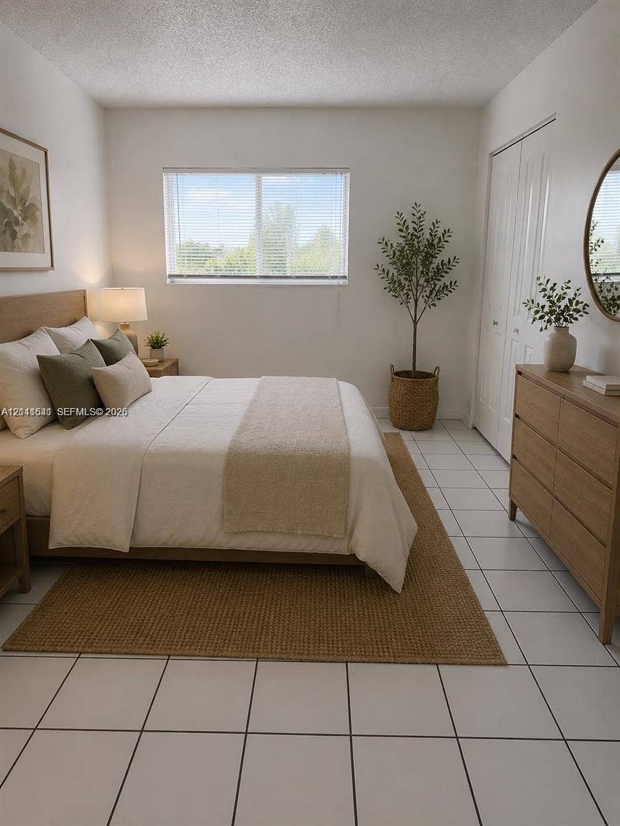 Room featuring light-colored tile flooring, a large window with blinds, and double-door closet storage