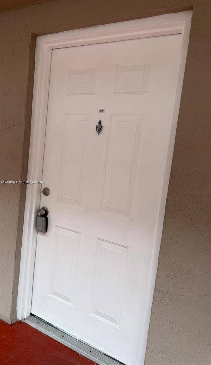 White six-panel entry door featuring a decorative metal door knocker and hardware
