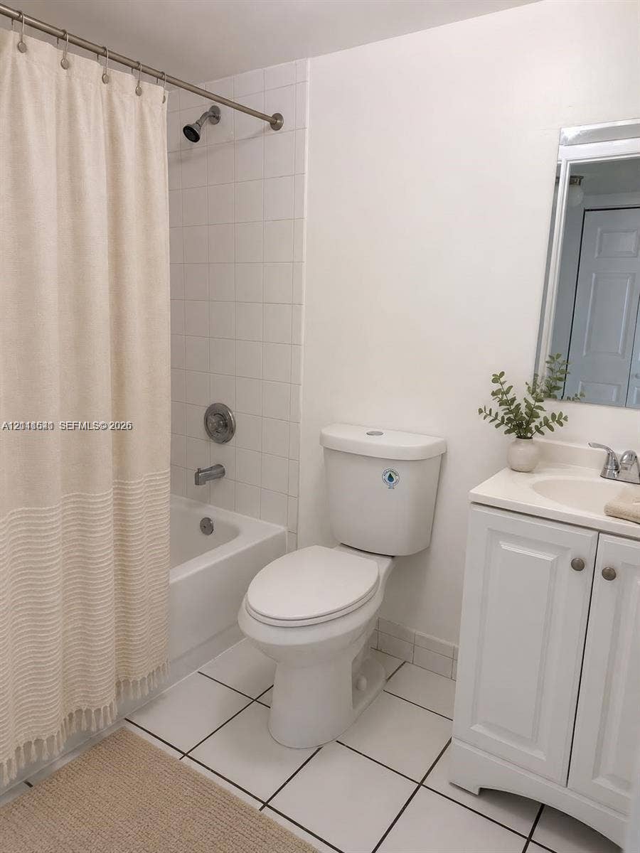 Bathroom featuring white tiled flooring, a bathtub with white tile surround, a single-sink vanity with white cabinetry, and a wall-mounted mirror