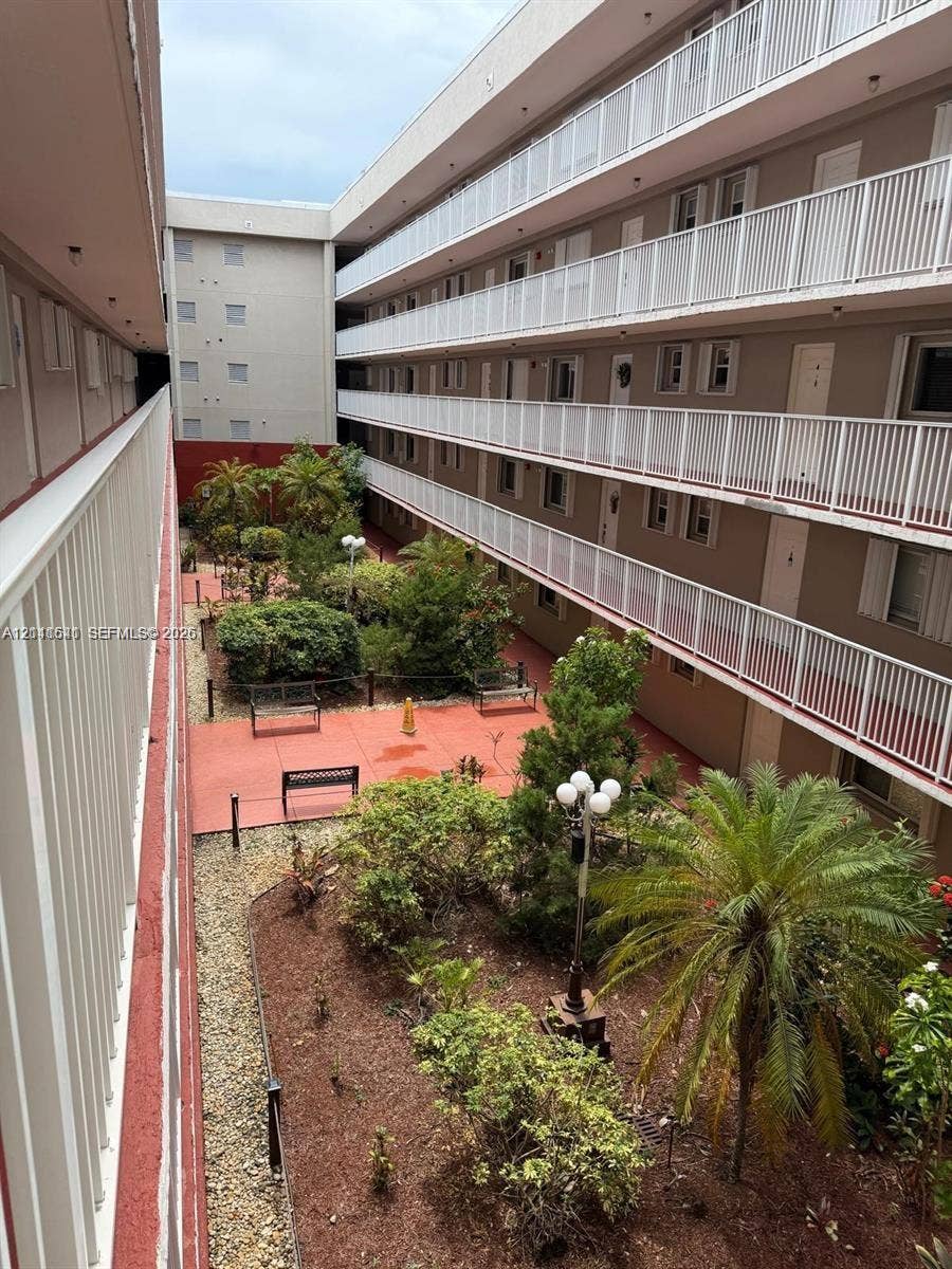 Exterior courtyard featuring multi-level white railed balconies, paved walkways, mature palm landscaping, and decorative outdoor lighting