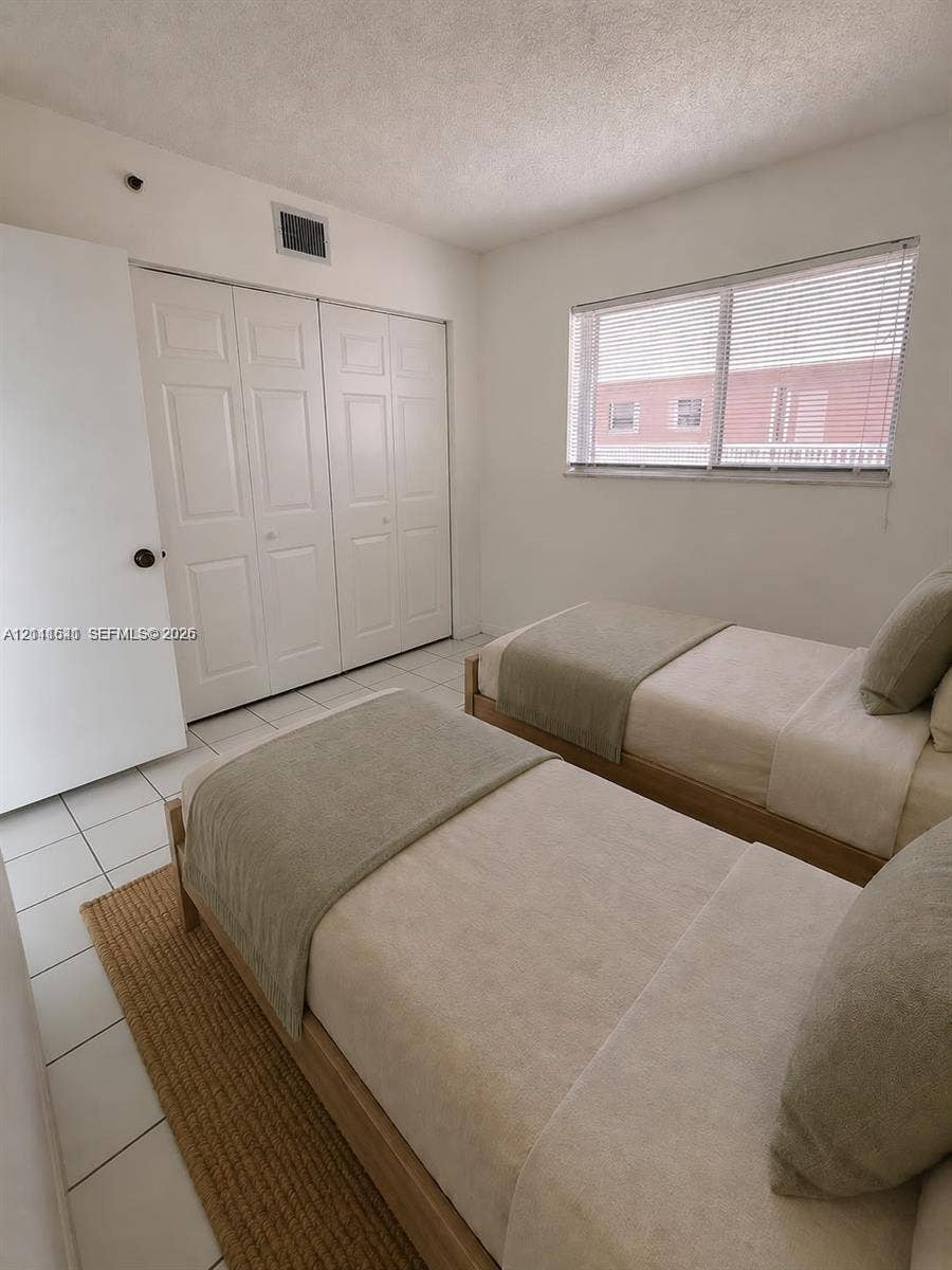 Neutral-toned room featuring ceramic tile flooring, a large window with horizontal blinds, and a built-in multi-panel closet