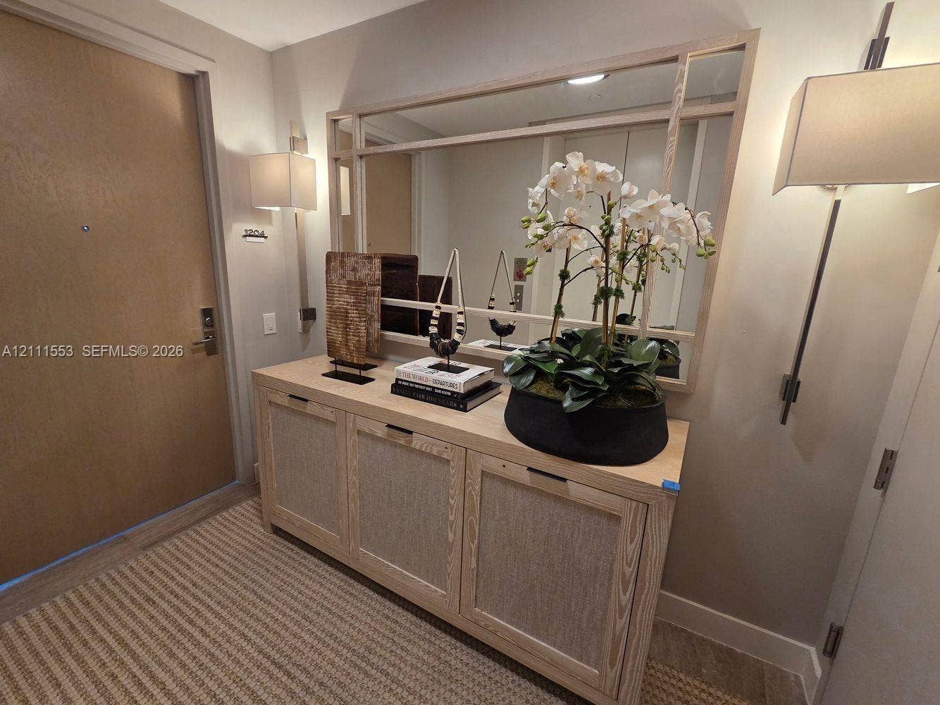 Built-in light-tone wood cabinetry with integrated hardware, framed wall-mounted mirror, and dual vertical wall sconces