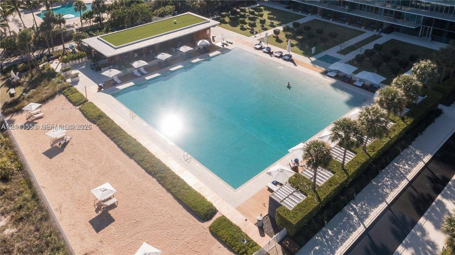 Expansive swimming pool featuring a large deck, perimeter landscaping, a covered pavilion, and dedicated sand area