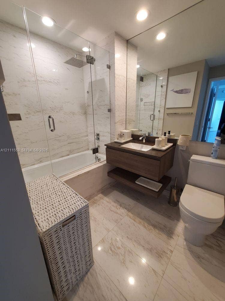 Full-height tiled shower surround with a frameless glass enclosure, rain-style showerhead, floating wood-finish vanity with an integrated basin, and large-format tile flooring