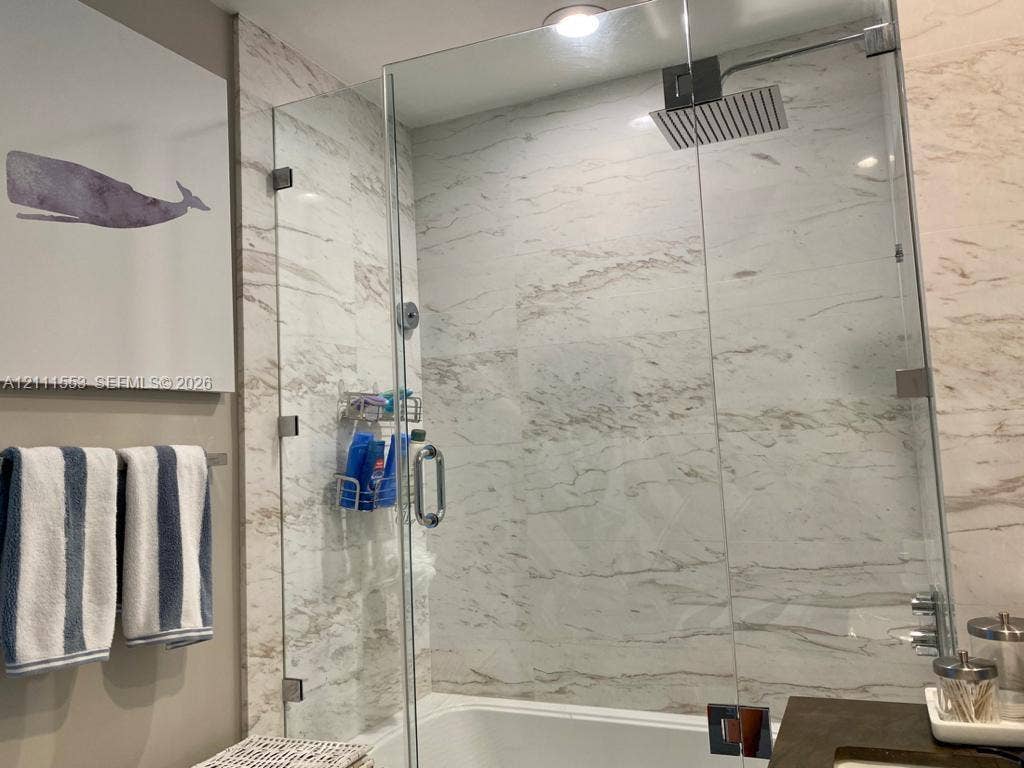 Walk-in shower featuring floor-to-ceiling stone-finish tile surround, a frameless glass enclosure, and a ceiling-mounted rainfall showerhead