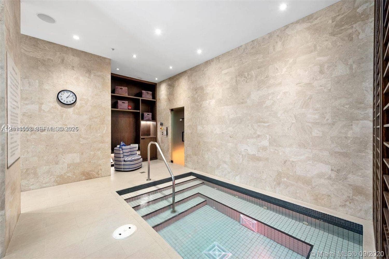 Indoor plunge pool featuring stone wall cladding, recessed lighting, built-in shelving, and a metal handrail
