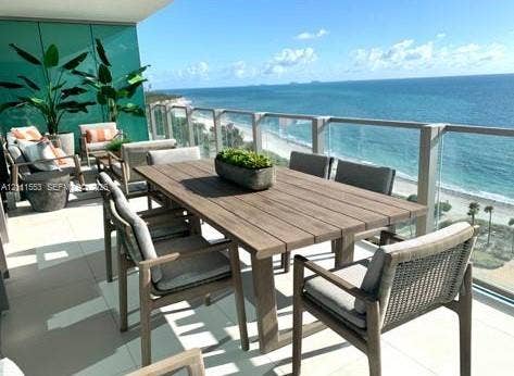 Covered balcony featuring oversized tile flooring, a glass panel railing, and ocean scenery
