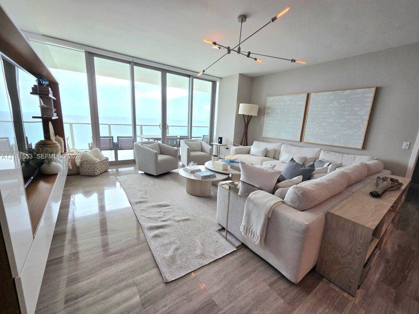 Floor-to-ceiling sliding glass doors, polished stone flooring, integrated wood-finish cabinetry, and contemporary multi-arm chandelier