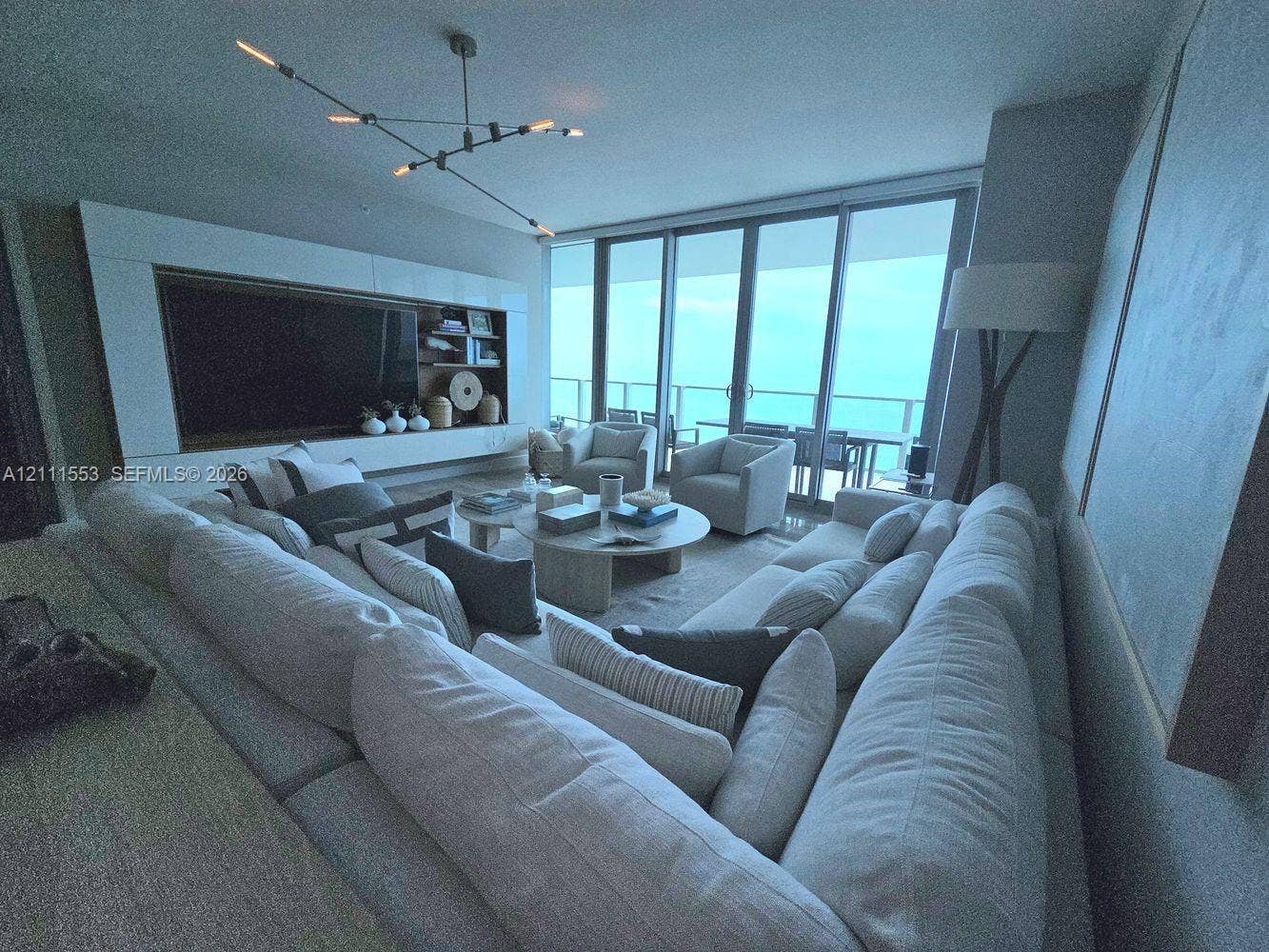 Floor-to-ceiling glass sliding doors, custom integrated media cabinetry, modern multi-arm chandelier, and stone flooring