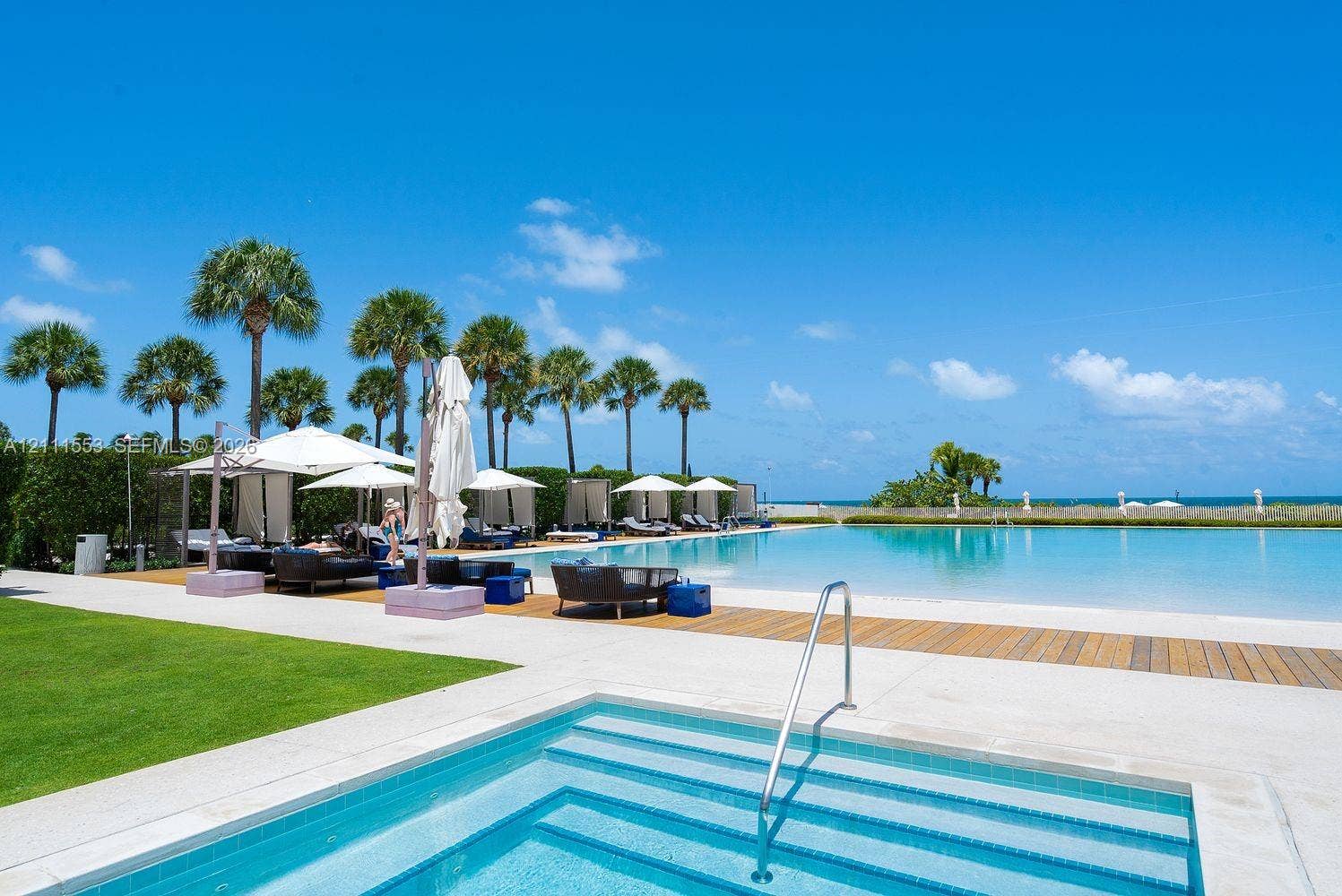 Swimming pool featuring a zero-entry design, integrated spa with submerged steps, expansive sun deck, and manicured lawn