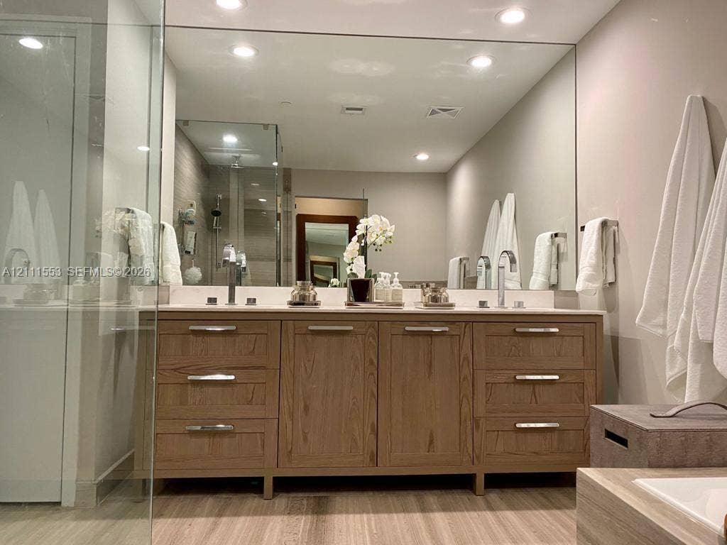 Double vanity featuring natural wood-finish cabinetry, chrome hardware, recessed lighting, and a full-width wall mirror