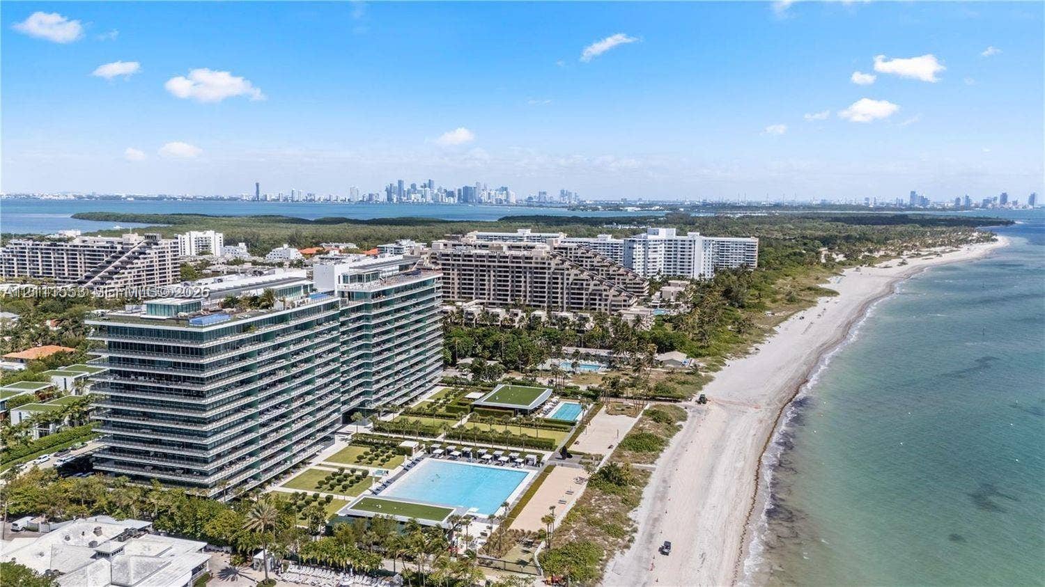 Aerial perspective of waterfront high-rise featuring expansive balconies, an outdoor swimming pool, landscaped grounds, and direct coastline access