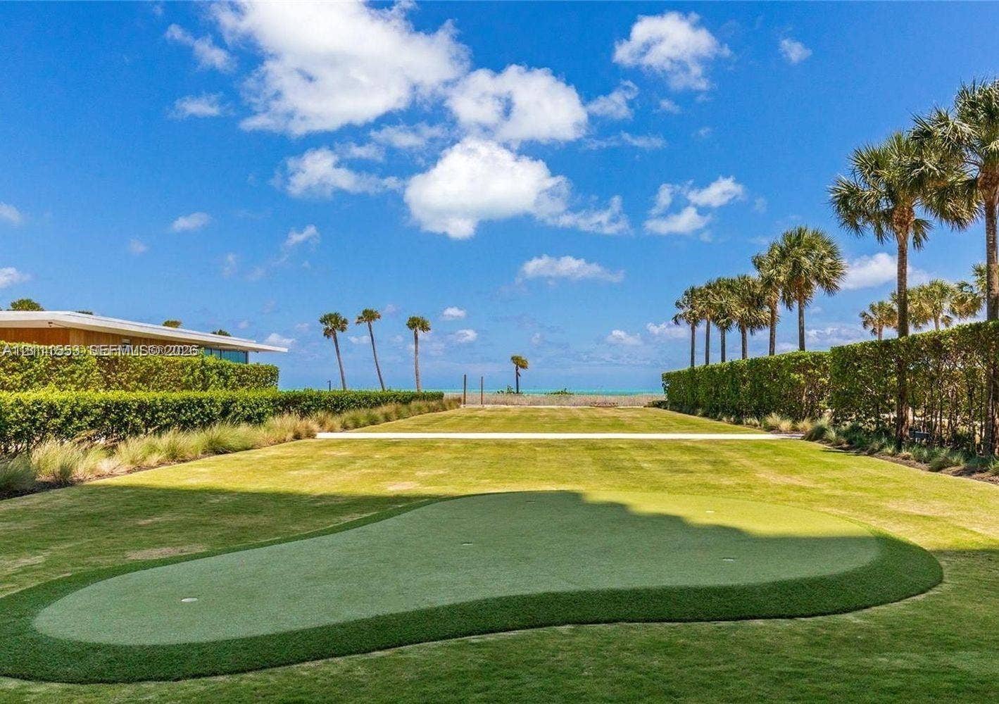 Expansive lawn featuring a built-in putting green, manicured hedge perimeter, and palm trees