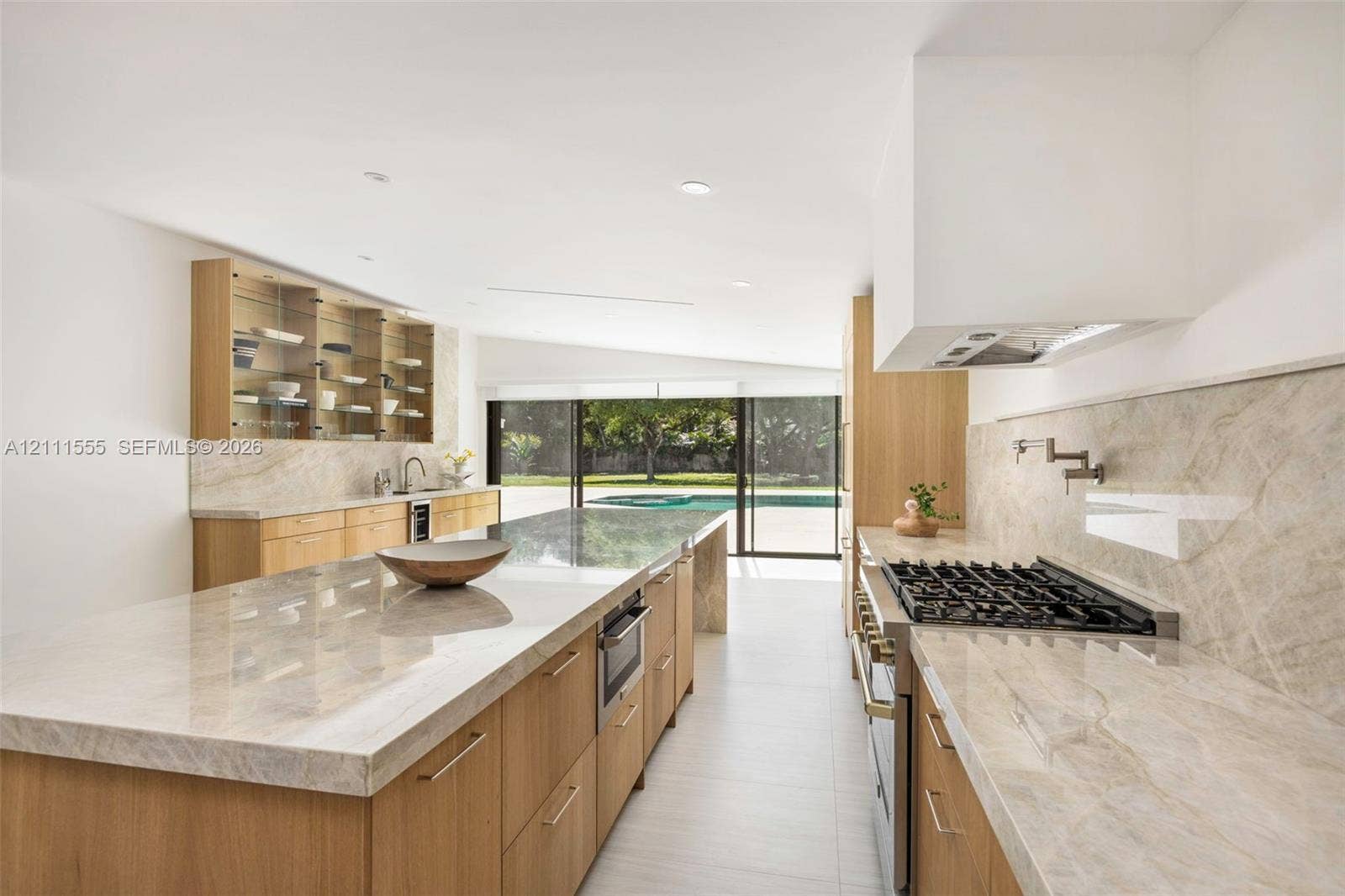 8800 SW 118th Street, Miami, Miami, FL 33176 Kitchen featuring light wood-finish cabinetry, natural stone countertops, a large center island, a built-in gas cooktop with pot filler, and glass-front upper displays