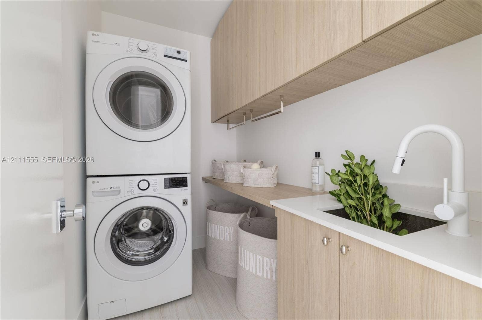 8800 SW 118th Street, Miami, Miami, FL 33176 Laundry space featuring stacked front-load laundry appliances, light wood-finish cabinetry, an under-mount sink, white solid-surface countertop, and wall-mounted white faucet