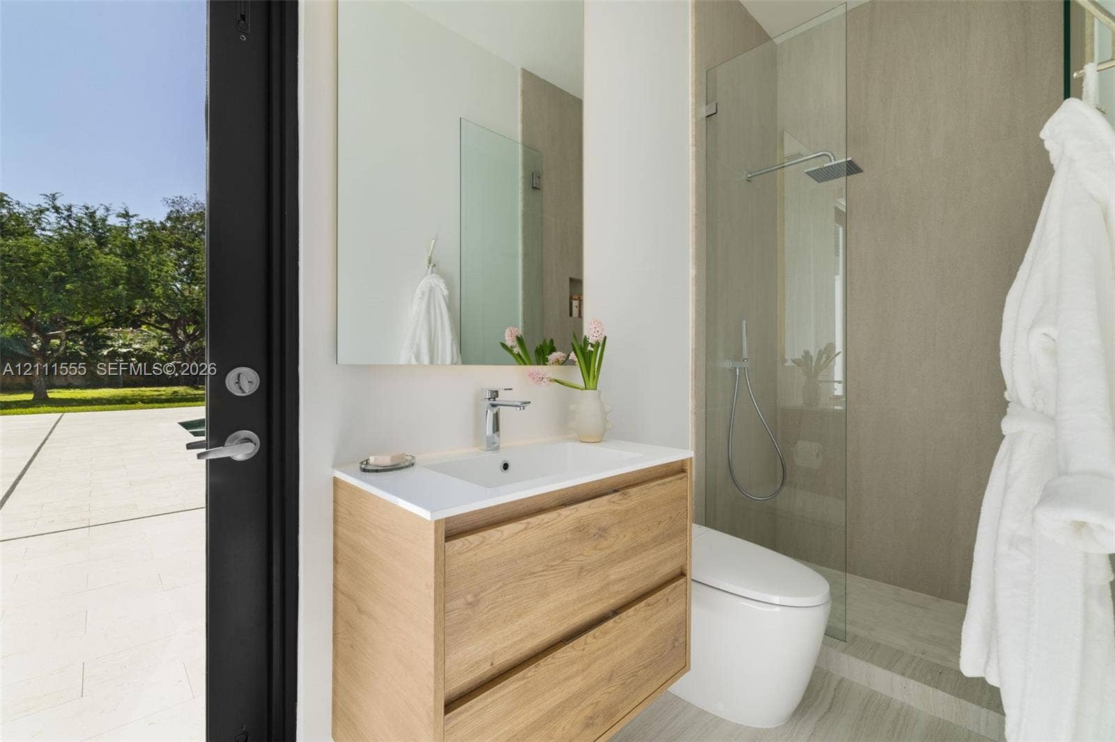 8800 SW 118th Street, Miami, Miami, FL 33176 Wall-mounted floating vanity with wood-finish cabinetry, rectangular integrated sink, frameless wall-to-wall mirror, glass-enclosed walk-in shower with rainfall showerhead, and porcelain tile flooring