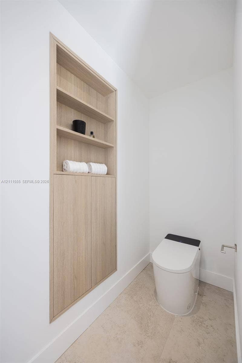8800 SW 118th Street, Miami, Miami, FL 33176 Built-in recessed wood-finish cabinetry featuring open shelving and lower storage cabinets, paired with a modern one-piece toilet and neutral stone-finish flooring