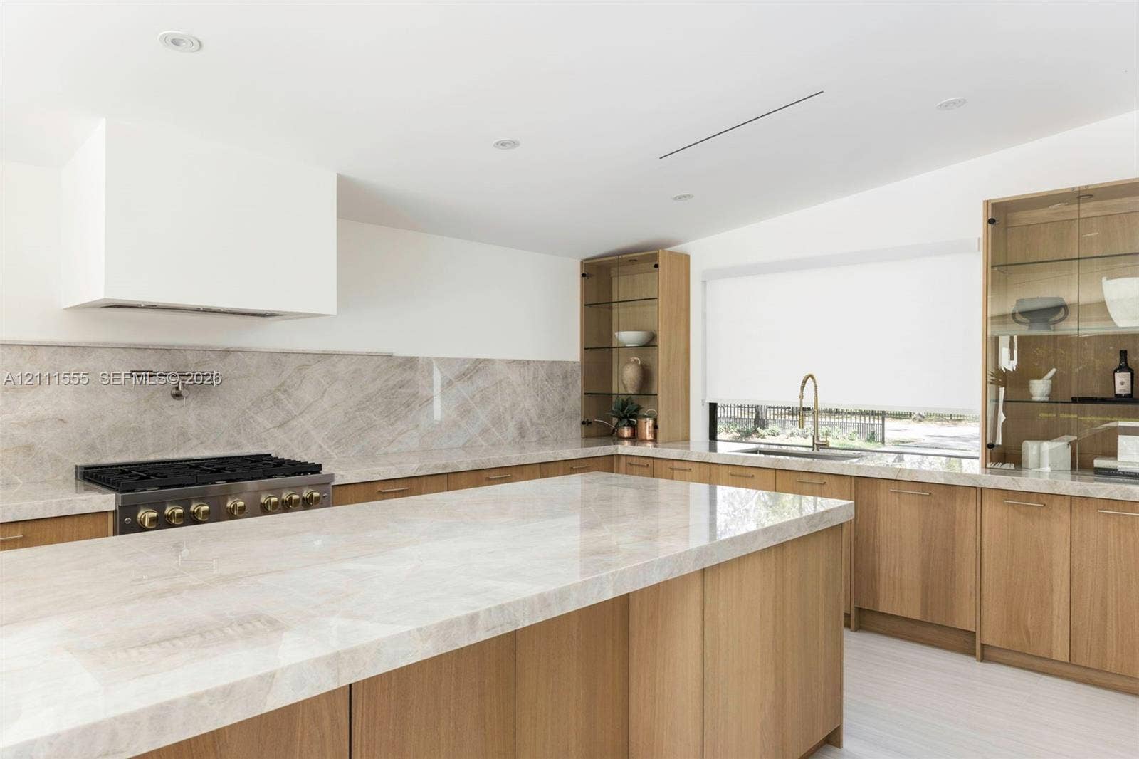 8800 SW 118th Street, Miami, Miami, FL 33176 Kitchen featuring natural wood cabinetry, stone-surface countertops and backsplash, integrated glass-front display shelving, wall-mounted pot filler, and a large central island