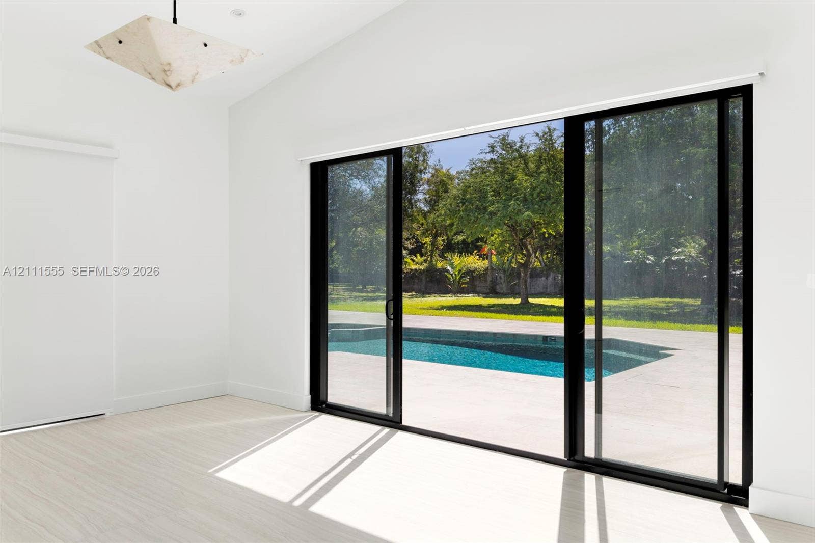 8800 SW 118th Street, Miami, Miami, FL 33176 Vaulted ceiling, geometric pendant lighting, light-toned flooring, and expansive black-framed sliding glass doors opening to an outdoor swimming pool and patio