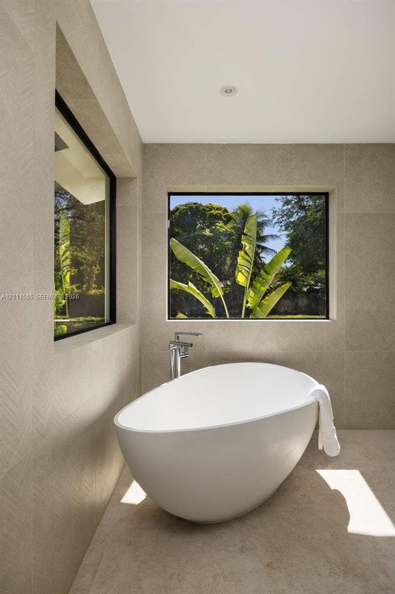 8800 SW 118th Street, Miami, Miami, FL 33176 Freestanding soaking tub featuring a chrome floor-mounted faucet, set against large-format neutral tile walls with textured herringbone detailing and recessed windows