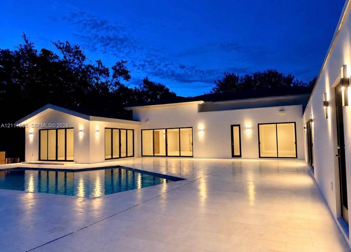 8800 SW 118th Street, Miami, Miami, FL 33176 Contemporary exterior featuring smooth stucco finish, expansive stone patio, integrated wall-mounted lighting, multiple sliding glass door sets, and a rectangular swimming pool