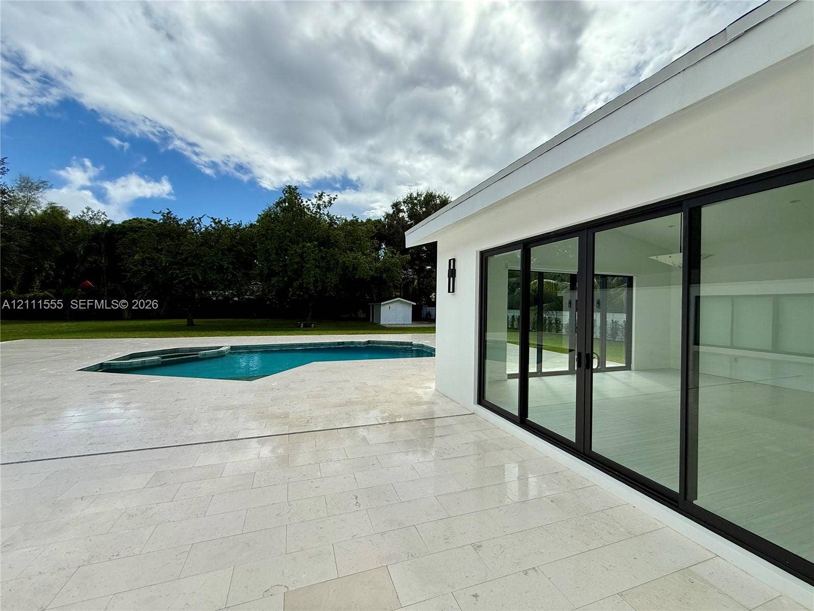 8800 SW 118th Street, Miami, Miami, FL 33176 Backyard featuring stone patio, in-ground swimming pool, and expansive sliding glass doors with black framing