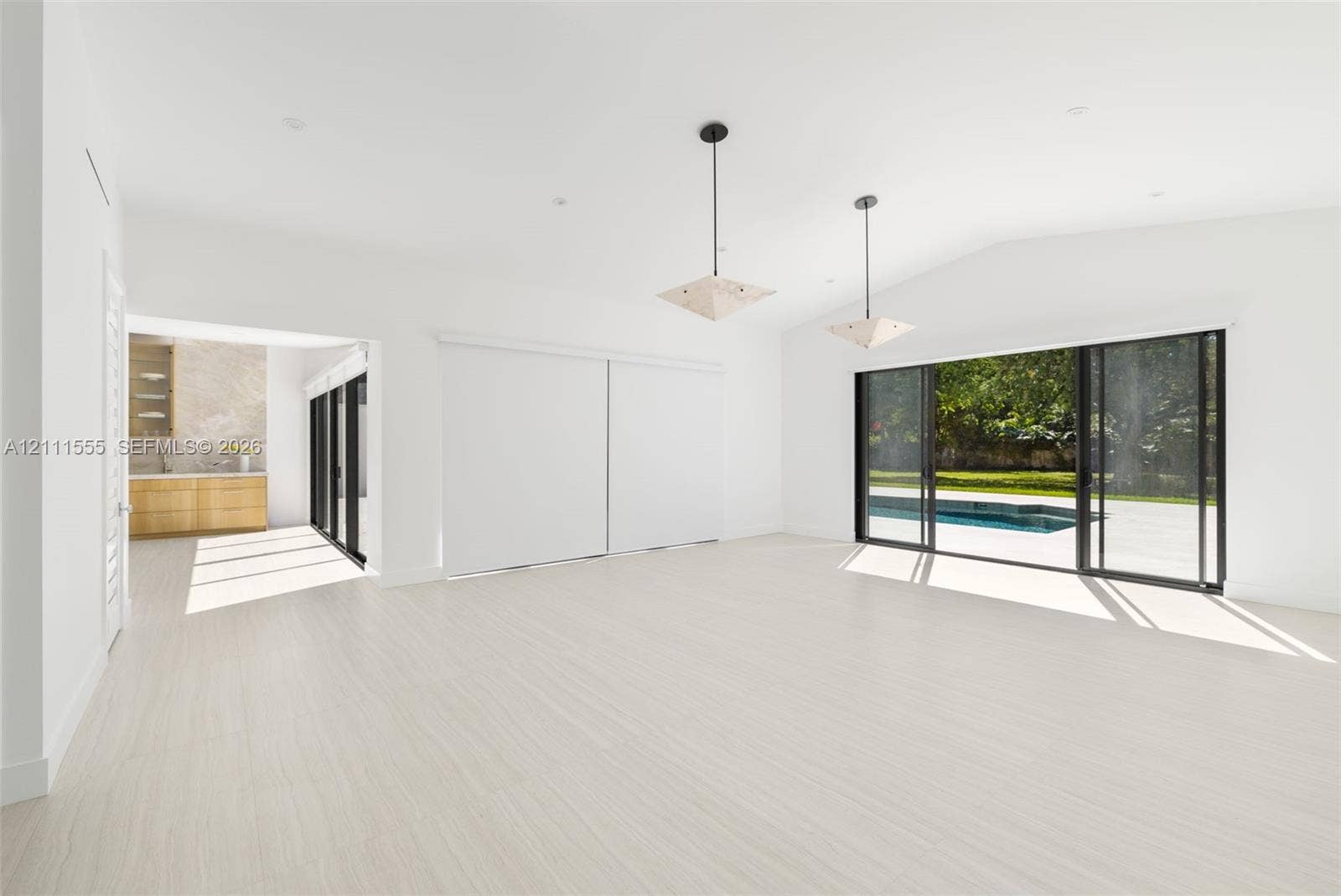 8800 SW 118th Street, Miami, Miami, FL 33176 Open living area featuring vaulted ceilings, wood-finish flooring, dual geometric pendant lighting, and multi-panel sliding glass doors with exterior pool access