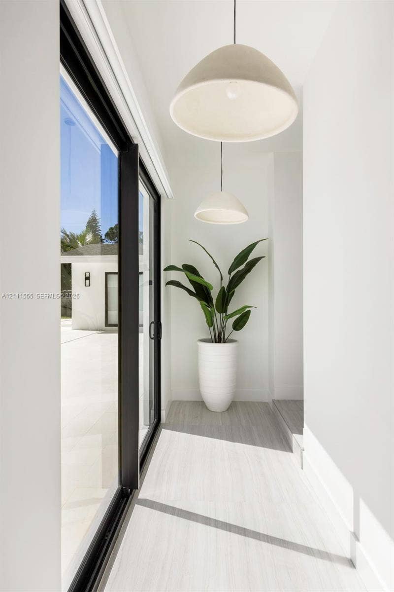 8800 SW 118th Street, Miami, Miami, FL 33176 Floor-to-ceiling sliding glass doors with black frames, neutral wood-finish flooring, and dual hemispherical pendant lighting fixtures