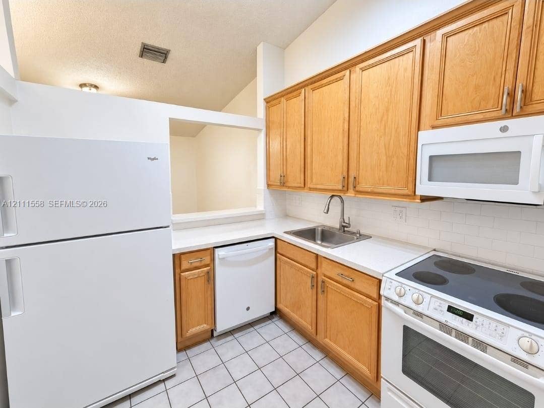 3652 NW 83rd Lane, #3652, Sunrise, Sunrise, FL 33351 Kitchen featuring natural wood cabinetry, white subway tile backsplash, white solid-surface countertops, ceramic tile flooring, and a stainless steel under-mount sink with a high-arch pull-down faucet