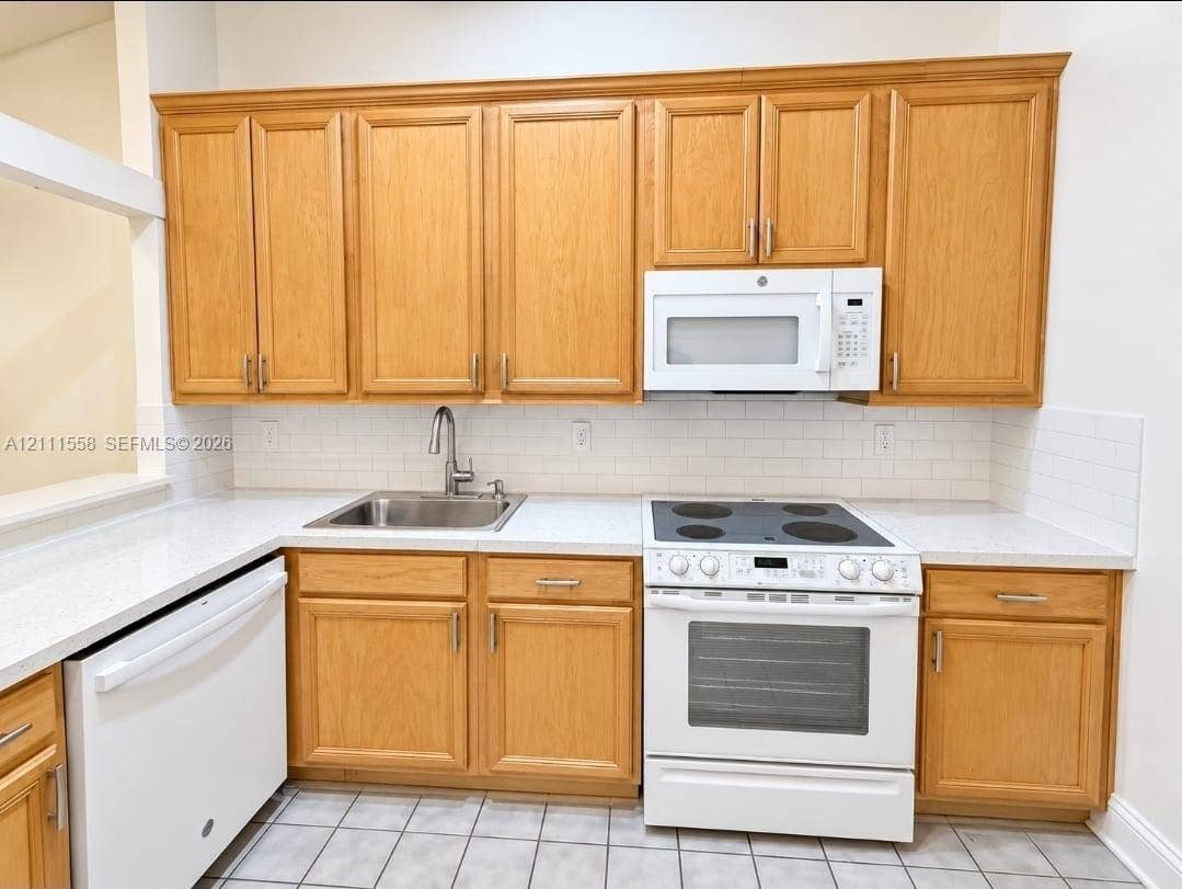 3652 NW 83rd Lane, #3652, Sunrise, Sunrise, FL 33351 Kitchen featuring light wood-finish cabinetry, white countertops, a white subway tile backsplash, a stainless steel undermount sink, and a white built-in microwave and range