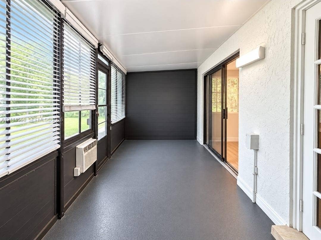 3652 NW 83rd Lane, #3652, Sunrise, Sunrise, FL 33351 Enclosed sunroom featuring expansive windows with horizontal blinds, textured white wall finishes, a solid flooring surface, a sliding glass door, and a dedicated wall-mounted climate control unit