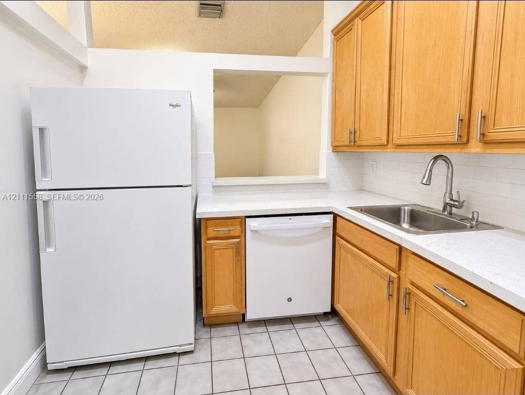 3652 NW 83rd Lane, #3652, Sunrise, Sunrise, FL 33351 Kitchen featuring wood cabinetry, white countertops, a stainless steel undermount sink with a gooseneck faucet, a white tile backsplash, and ceramic floor tiling