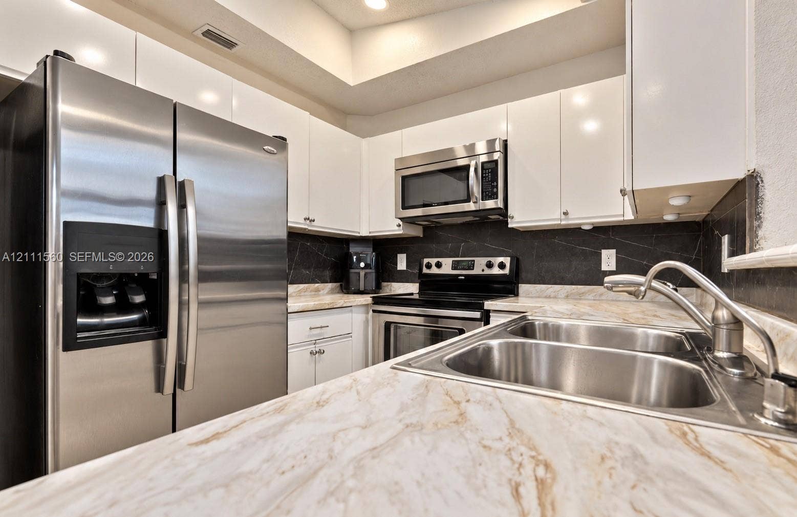 3539 W Inverrary Boulevard W, #1, Lauderhill, Lauderhill, FL 33319 Kitchen featuring white gloss cabinetry, stone-patterned countertops, stainless steel appliances, and a dark stone-finish backsplash with an integrated dual-basin stainless steel sink