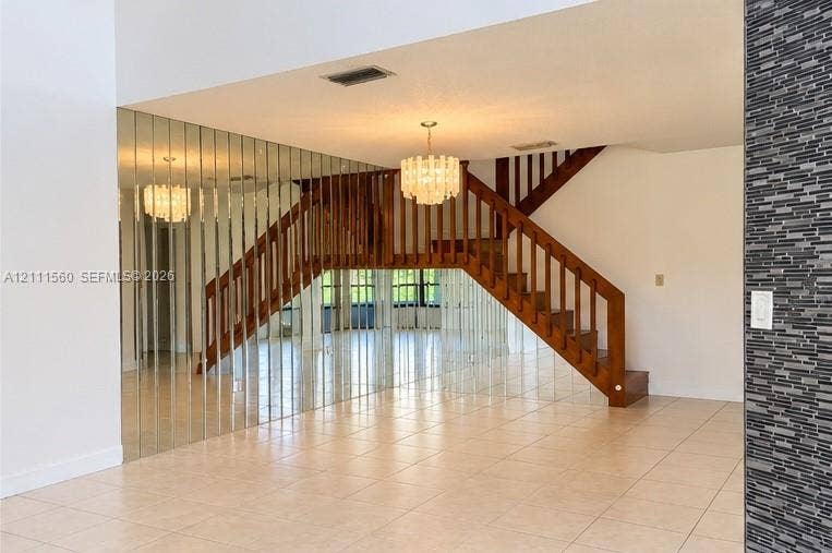3539 W Inverrary Boulevard W, #1, Lauderhill, Lauderhill, FL 33319 Staircase featuring wood railings and vertical balusters, mirrored accent wall, tiled flooring, tiered glass chandelier, and textured stone-finish wall accent