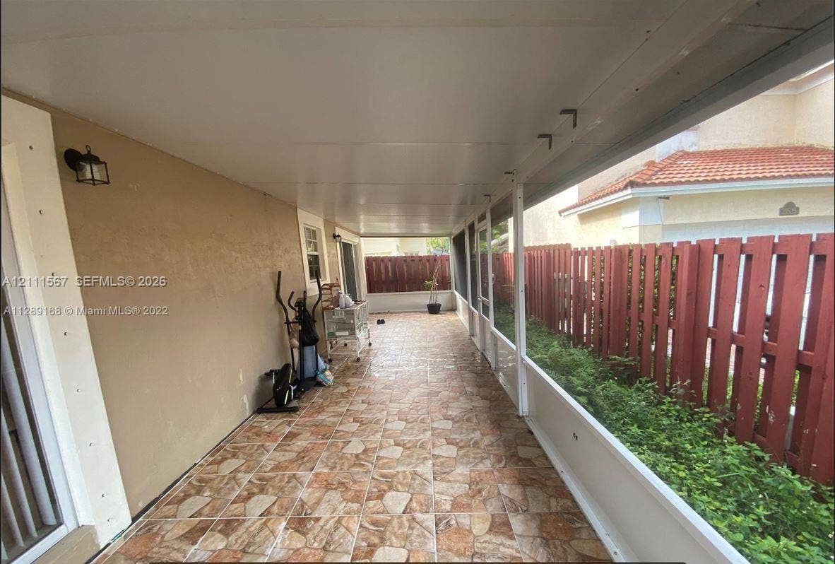 21514 SW 90th Avenue, Cutler Bay, FL 33189 Covered patio featuring stone-patterned tile flooring, a solid ceiling with attached wall-mounted lighting, and screen panel enclosures bordered by a wood-slat fence