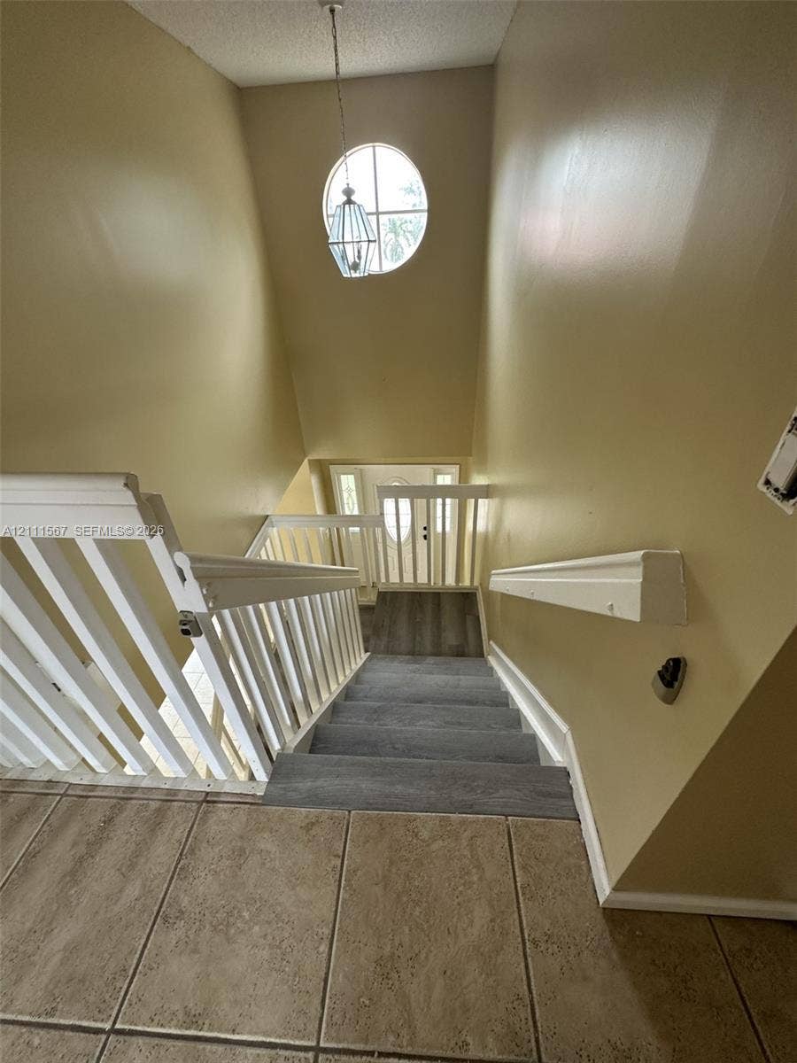 21514 SW 90th Avenue, Cutler Bay, FL 33189 Staircase featuring white balustrades, carpeted treads, a circular accent window, and a hanging pendant light fixture