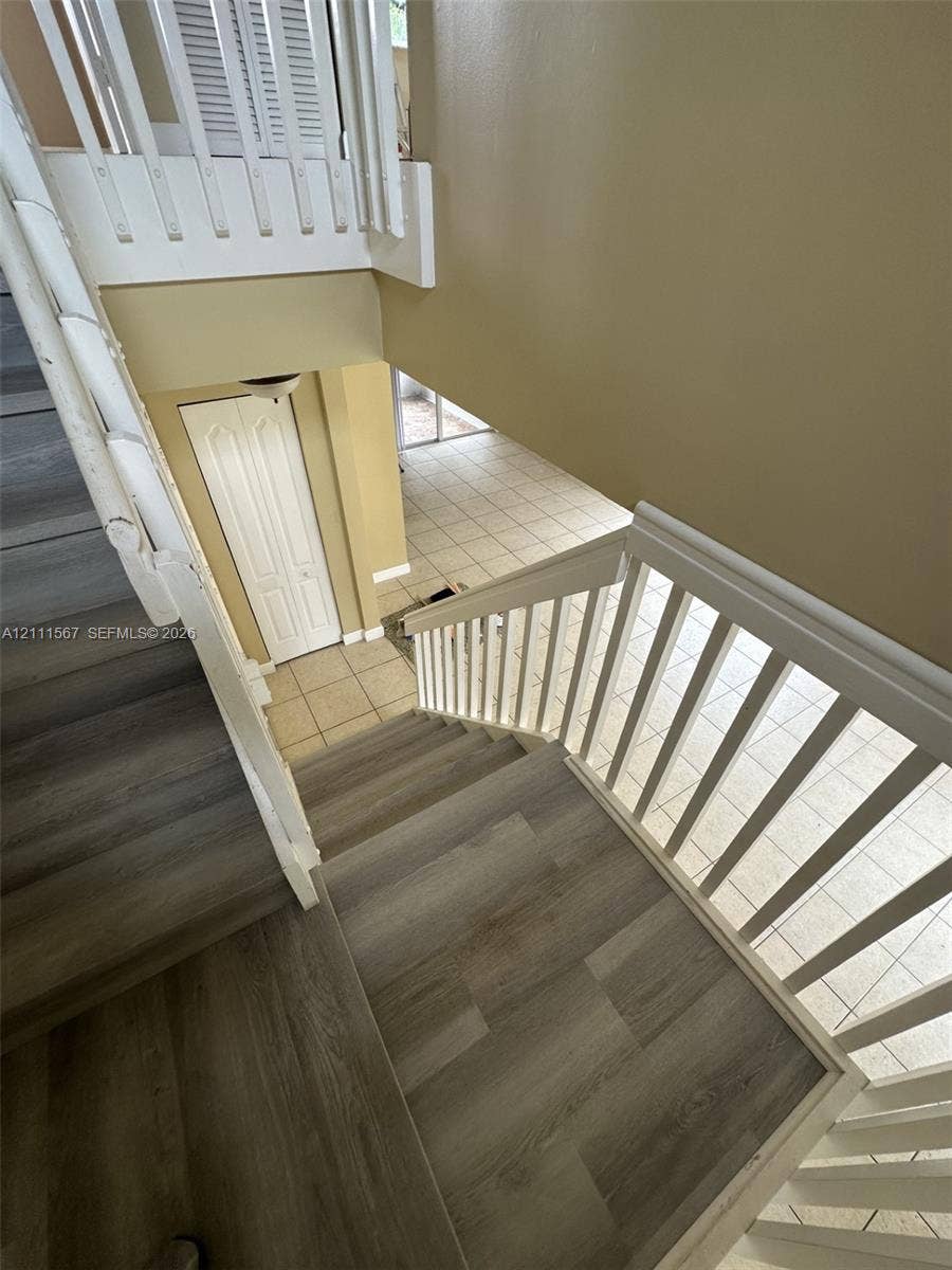 21514 SW 90th Avenue, Cutler Bay, FL 33189 Staircase featuring wood-finish flooring, white wooden balustrades, and ceramic tile flooring on the ground level