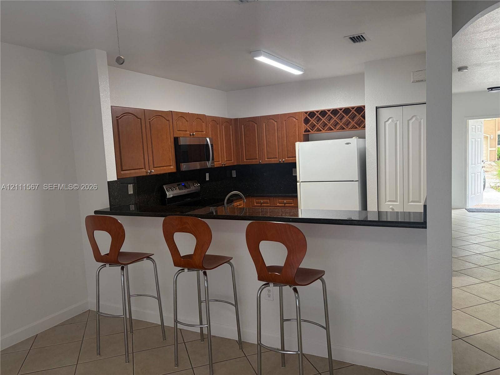 21514 SW 90th Avenue, Cutler Bay, FL 33189 Kitchen featuring dark stone countertops, wood-finish cabinetry, a built-in wine rack, and a breakfast bar