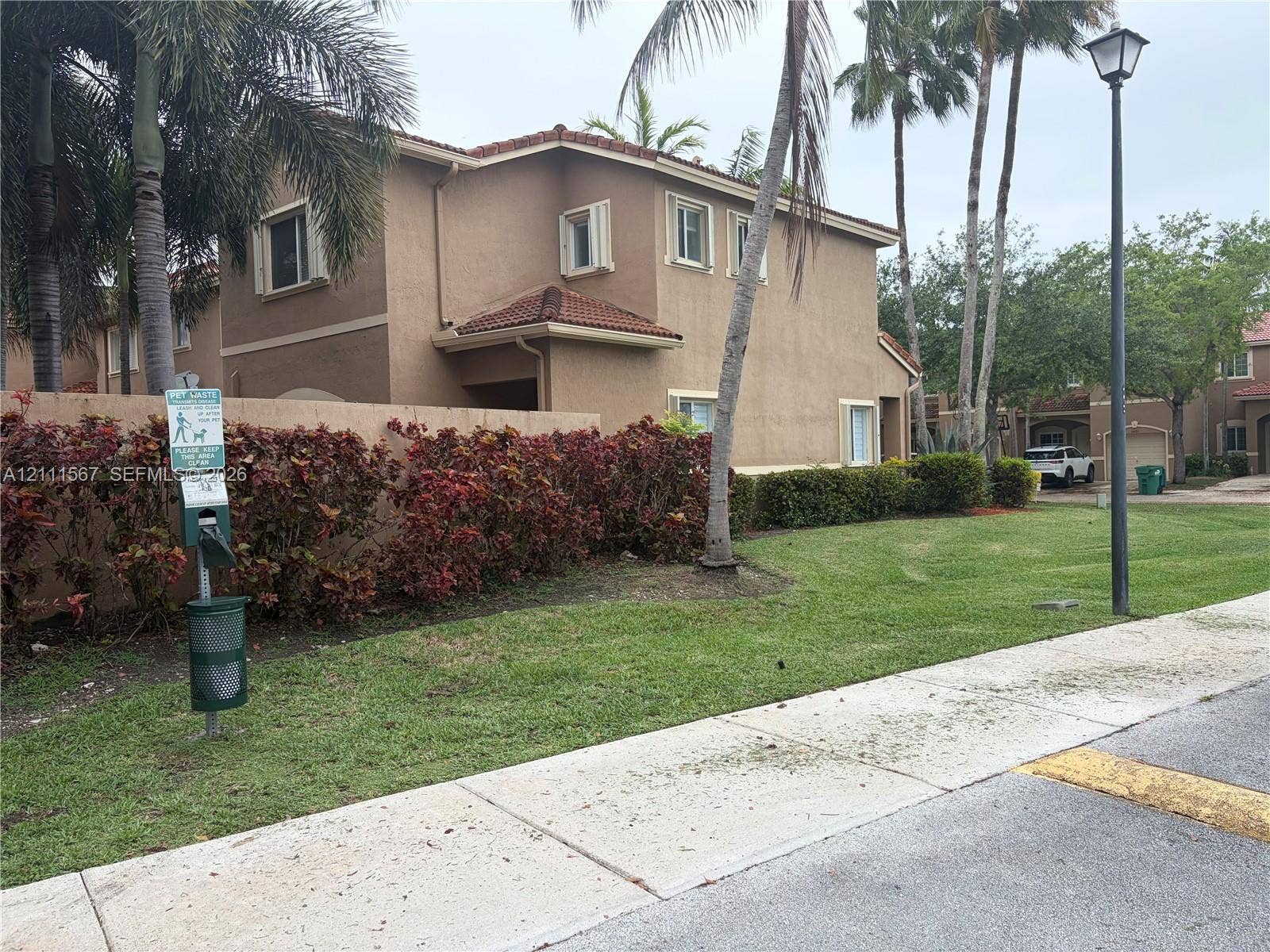 21514 SW 90th Avenue, Cutler Bay, FL 33189 Two-story stucco exterior featuring a tile roof, mature palm trees, landscaped shrubbery, and a concrete sidewalk