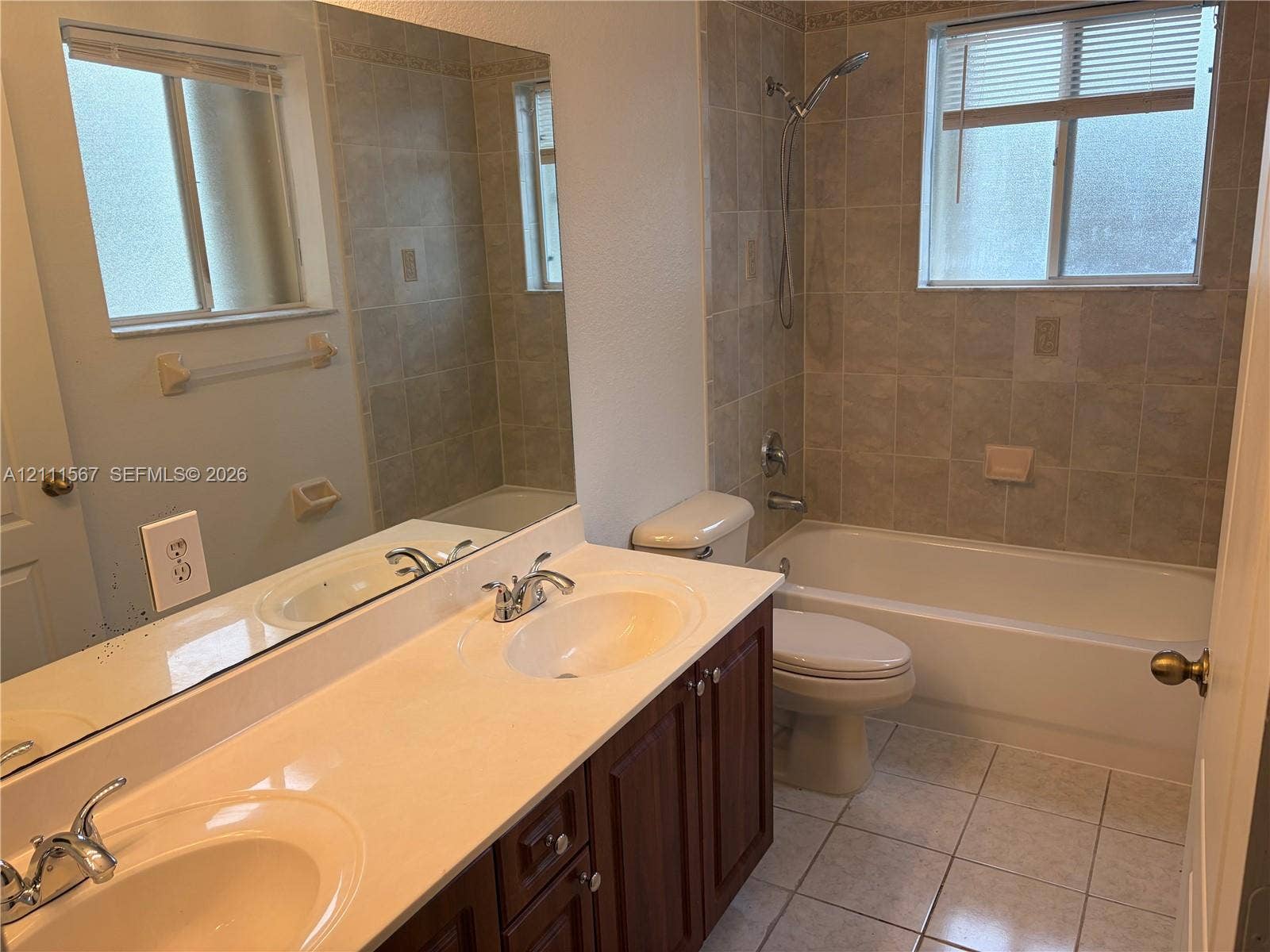 21514 SW 90th Avenue, Cutler Bay, FL 33189 Double-sink vanity with a solid-surface countertop, dark wood-finish cabinetry, ceramic tile flooring, and a shower-tub combination featuring full-height wall tiling