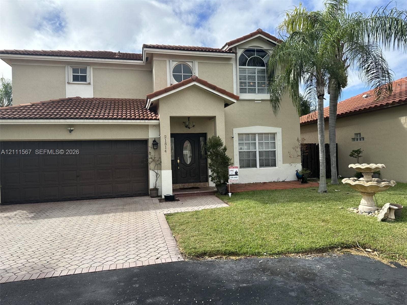 21514 SW 90th Avenue, Cutler Bay, FL 33189 Two-story exterior featuring a stucco facade, tile roof, arched window detailing, paver driveway, and a front garden fountain