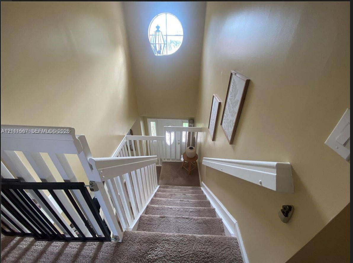 21514 SW 90th Avenue, Cutler Bay, FL 33189 Staircase featuring white balusters, a wooden handrail, carpeted steps, and a circular accent window