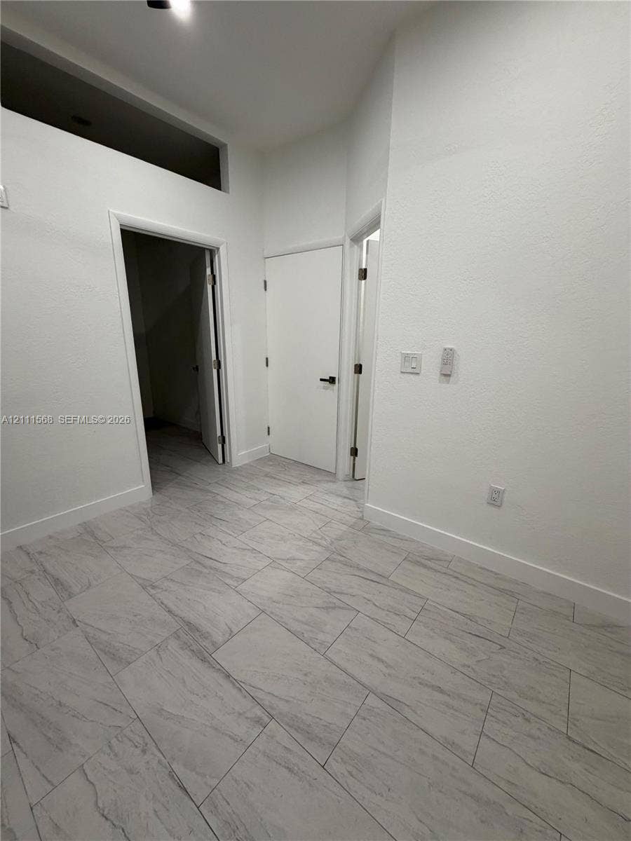 Neutral interior featuring large-format stone-finish floor tiling, high ceilings with a transom window, and solid-core doors with matte black hardware