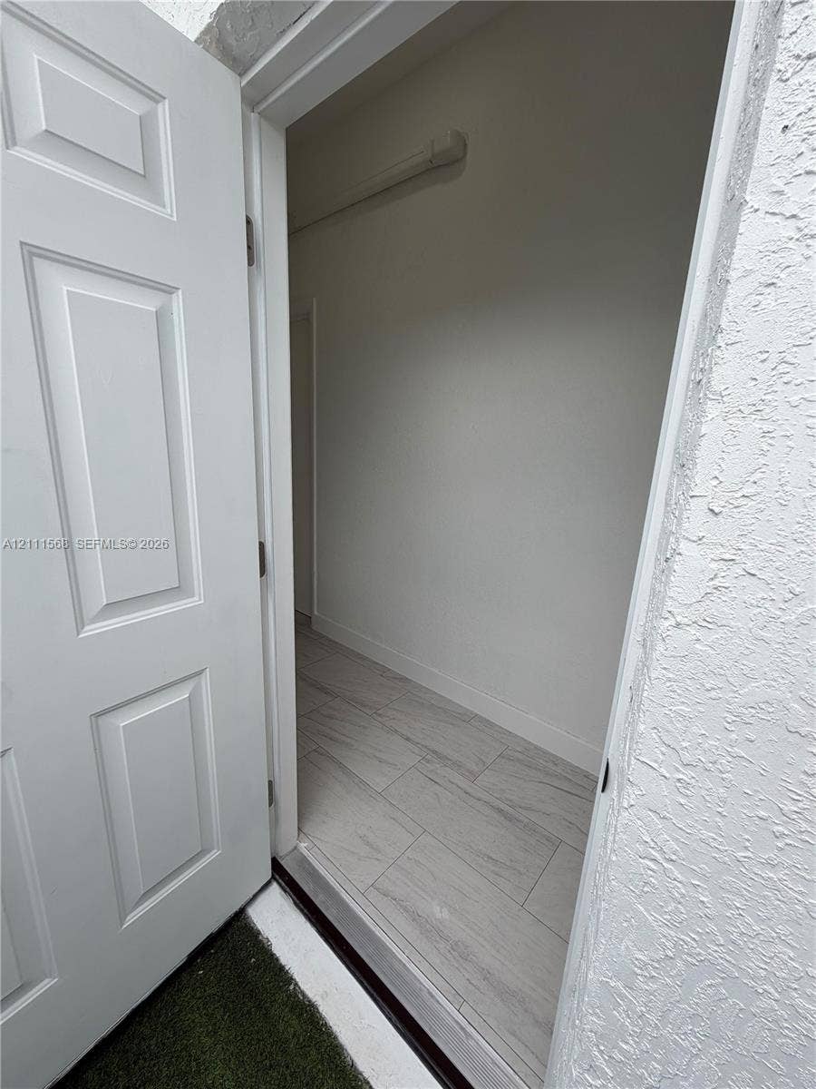 Six-panel interior door with light-colored wood-finish flooring and textured stucco exterior wall