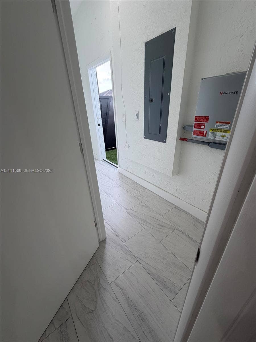 Light-toned ceramic tile flooring, textured wall finishes, and integrated electrical service panel with energy monitoring equipment