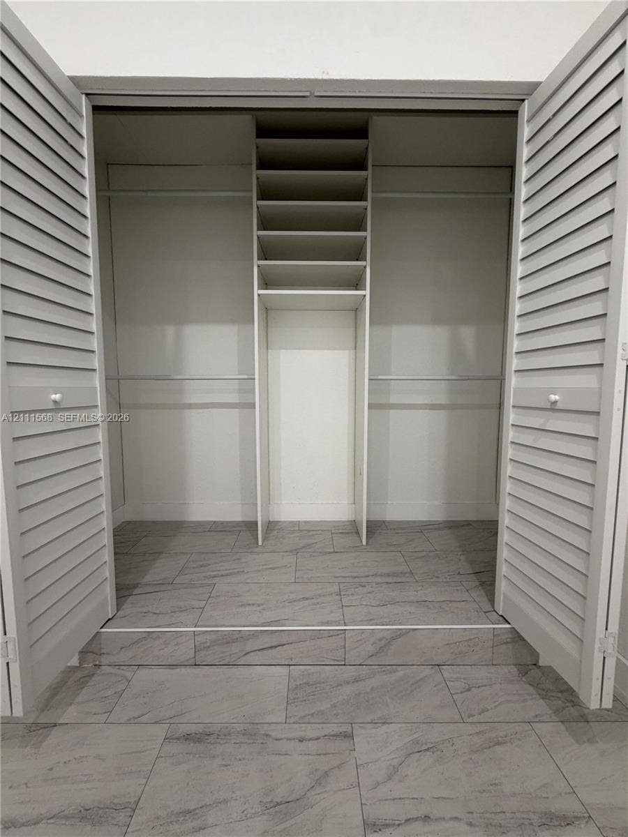 Closet featuring louvered bifold doors, tile flooring, built-in shelving, and dual hanging rods