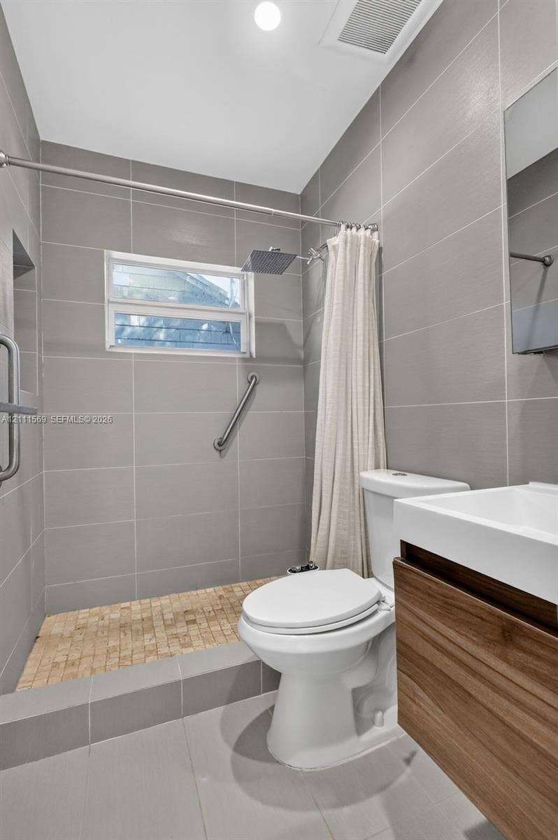 12800 NE 11th Avenue, #4, North Miami, North Miami, FL 33161 Bathroom featuring floor-to-ceiling grey tile walls, a walk-in shower with mosaic tile flooring, a wood-finish floating vanity, and a rectangular vessel sink